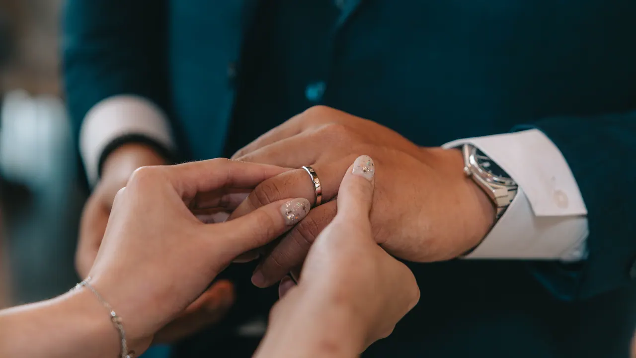 A ring slipped onto the groom’s finger, close up.