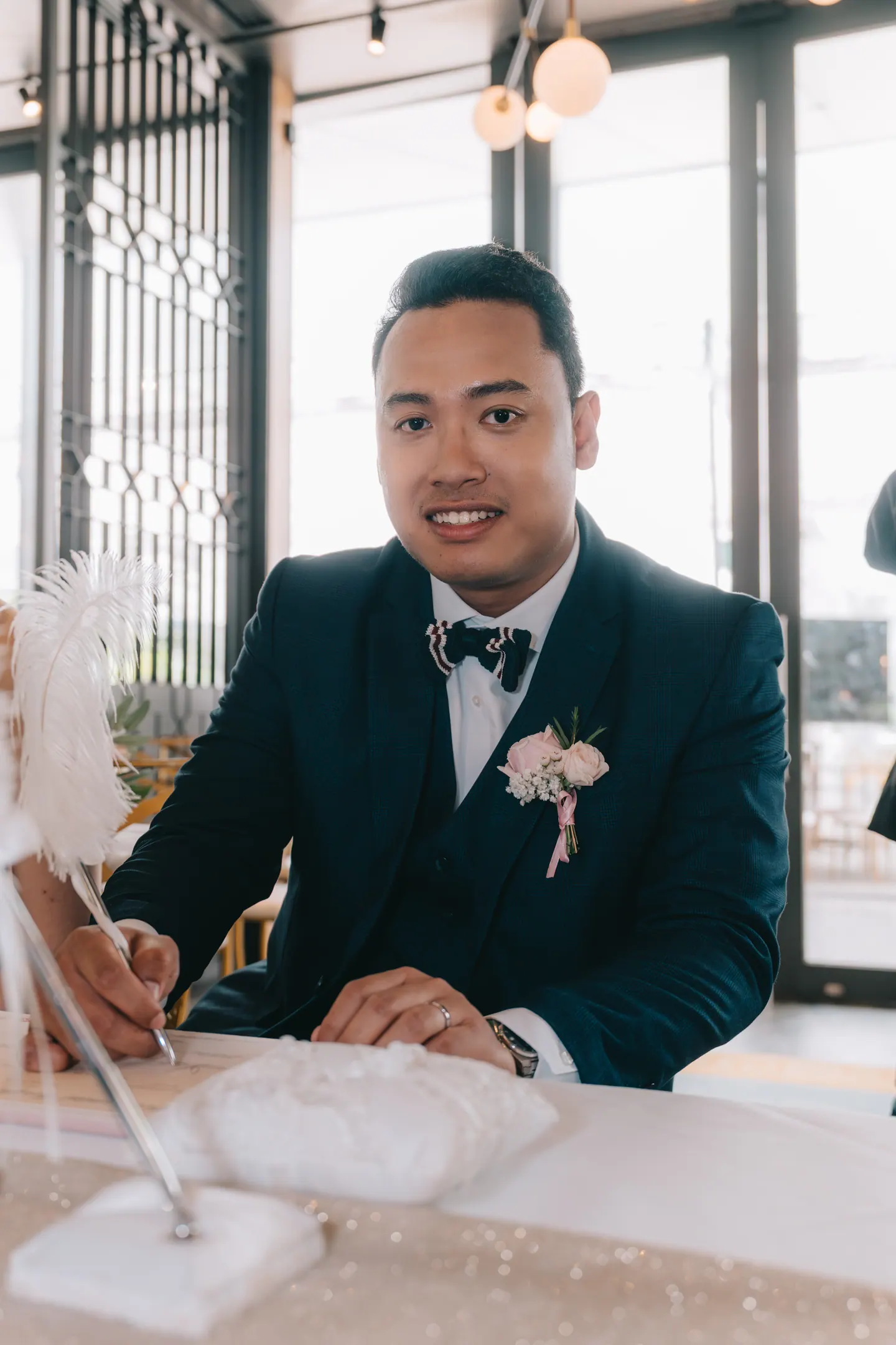 The groom signs at the table and smiles up.