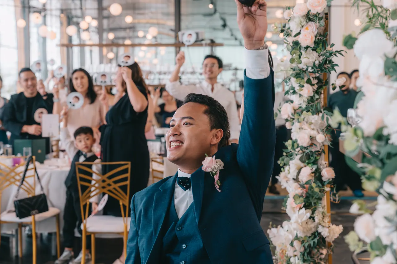 The groom raises his arm as guests cheer behind him.