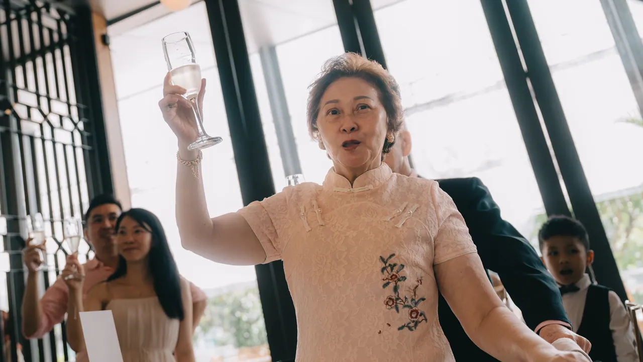 An older woman raises her glass high.