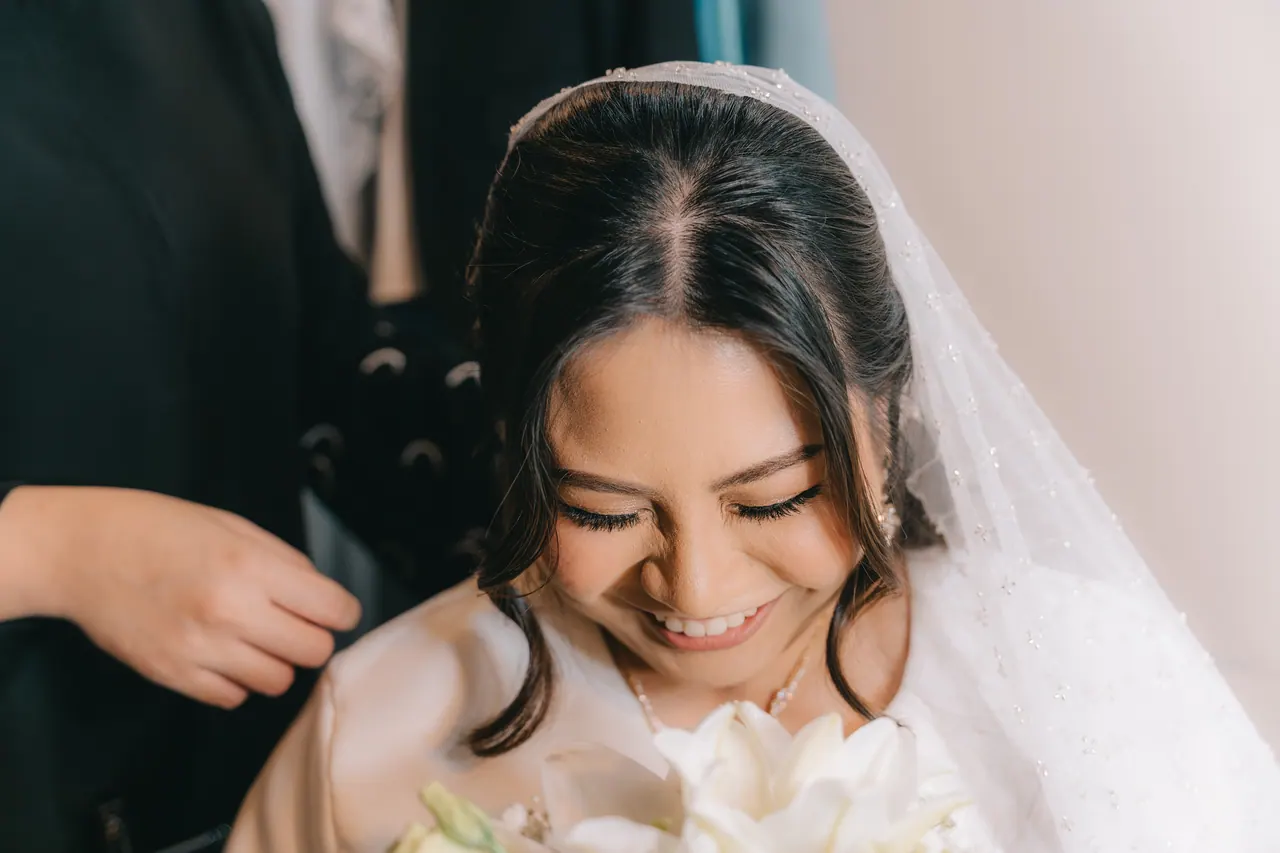 The bride looks down and smiles as her veil is set.