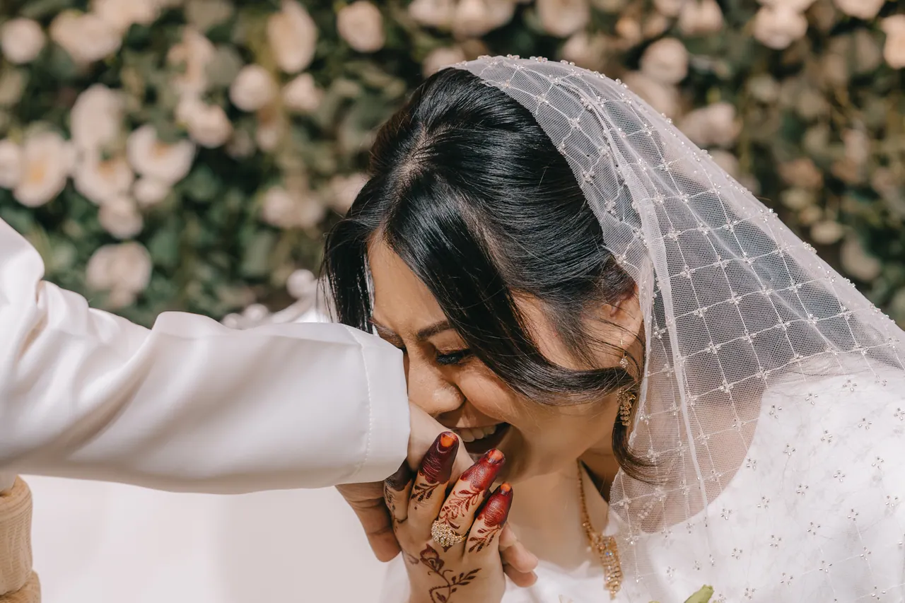 The bride kisses the groom’s hand, her hands painted with henna.