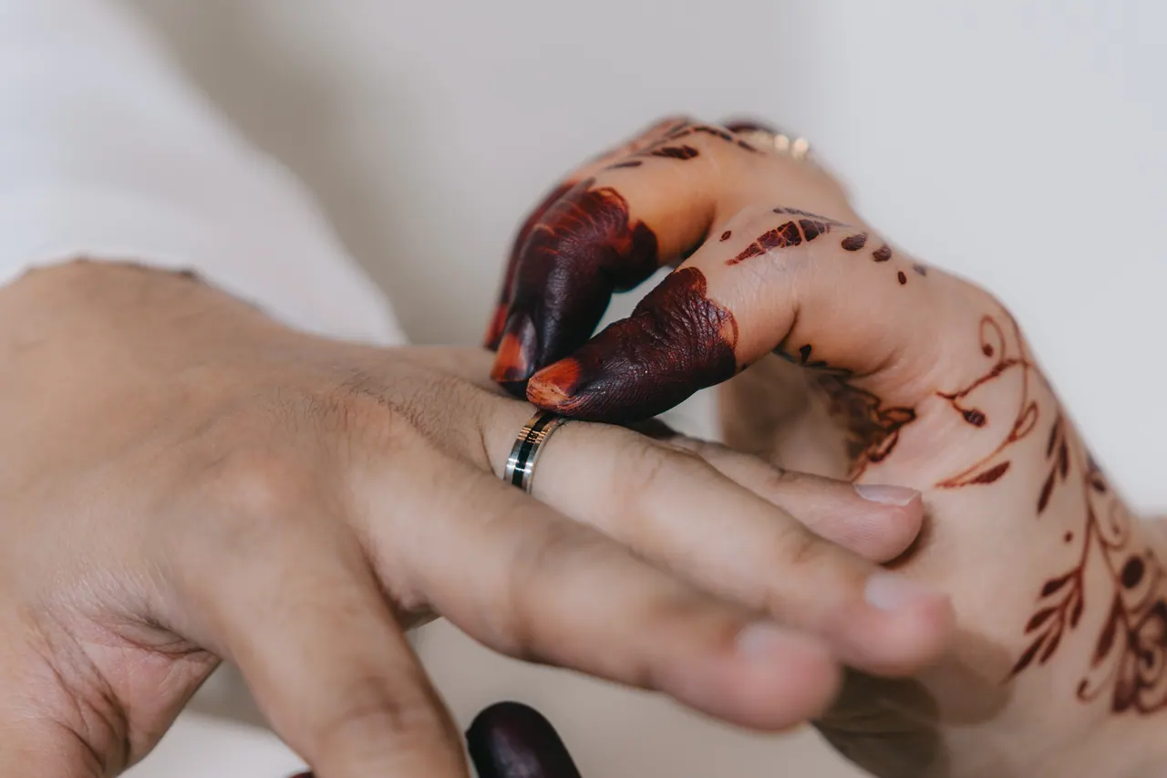 A hennaed hand slides a ring onto the groom’s finger.