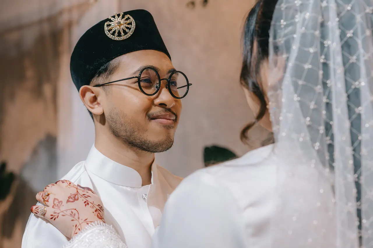 The groom smiles, the bride’s hennaed hand on his shoulder.