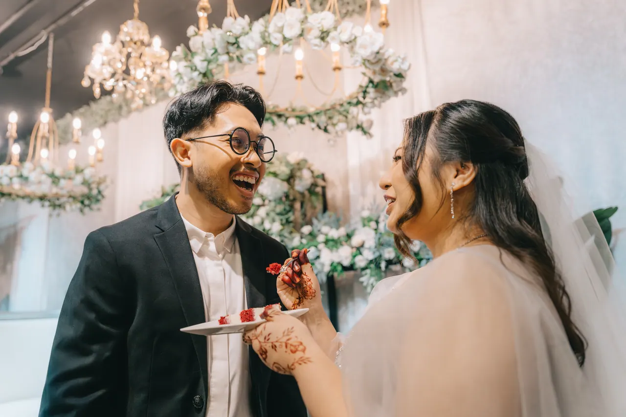 The couple feed each other cake under chandeliers.