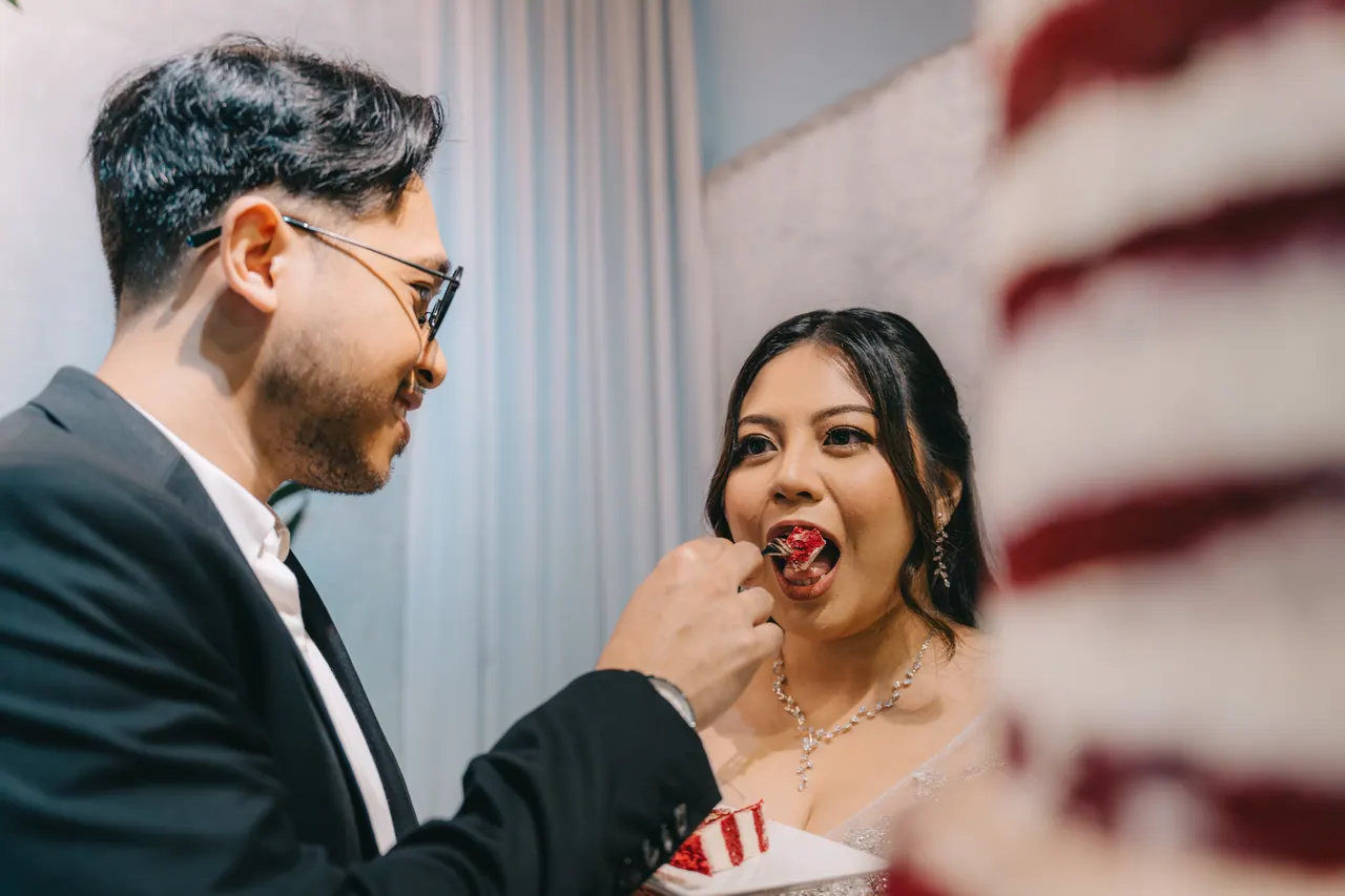 The groom feeds the bride a bite of red velvet cake.