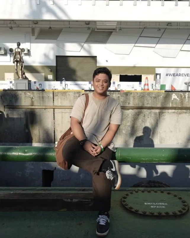 Khai, sitting on a green railing by the water in the late afternoon sun, smiling at the camera.