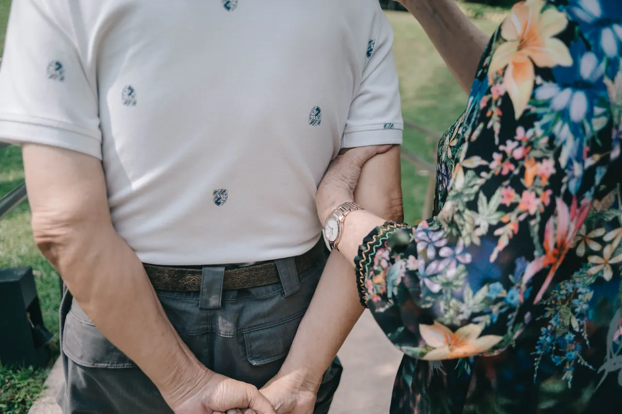 An older couple hold hands, close up.