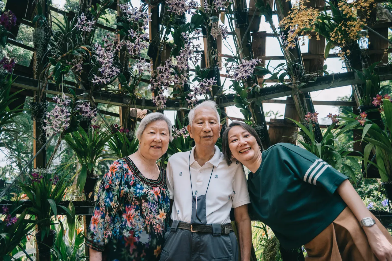 An older couple and their daughter under orchids.
