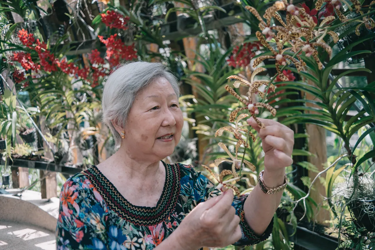 An older woman smiles among the orchids.