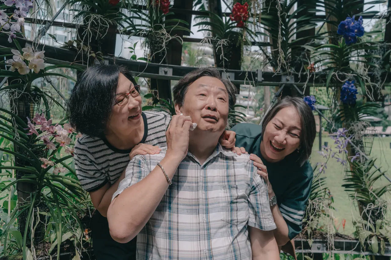 An older man laughs as two women pinch his cheeks.