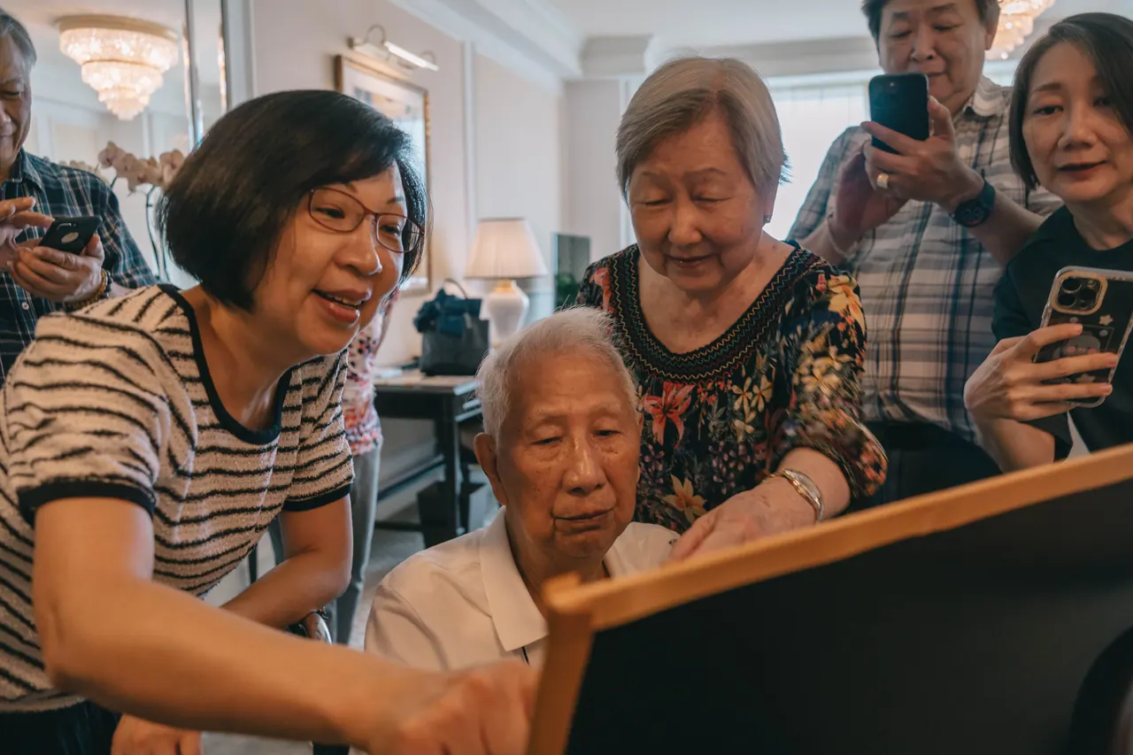 Family gather round an older woman to read a card.