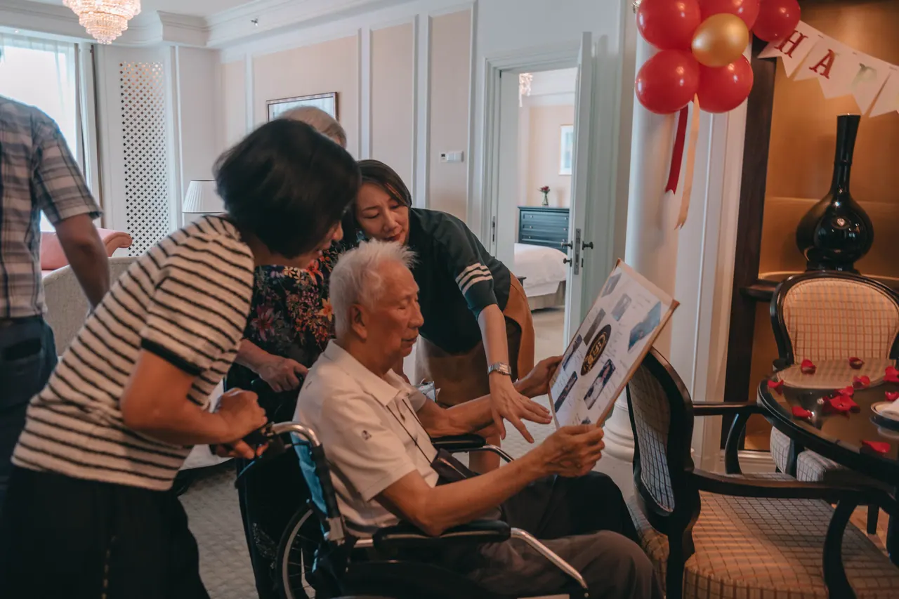 Family lean over an older man to show him a card.