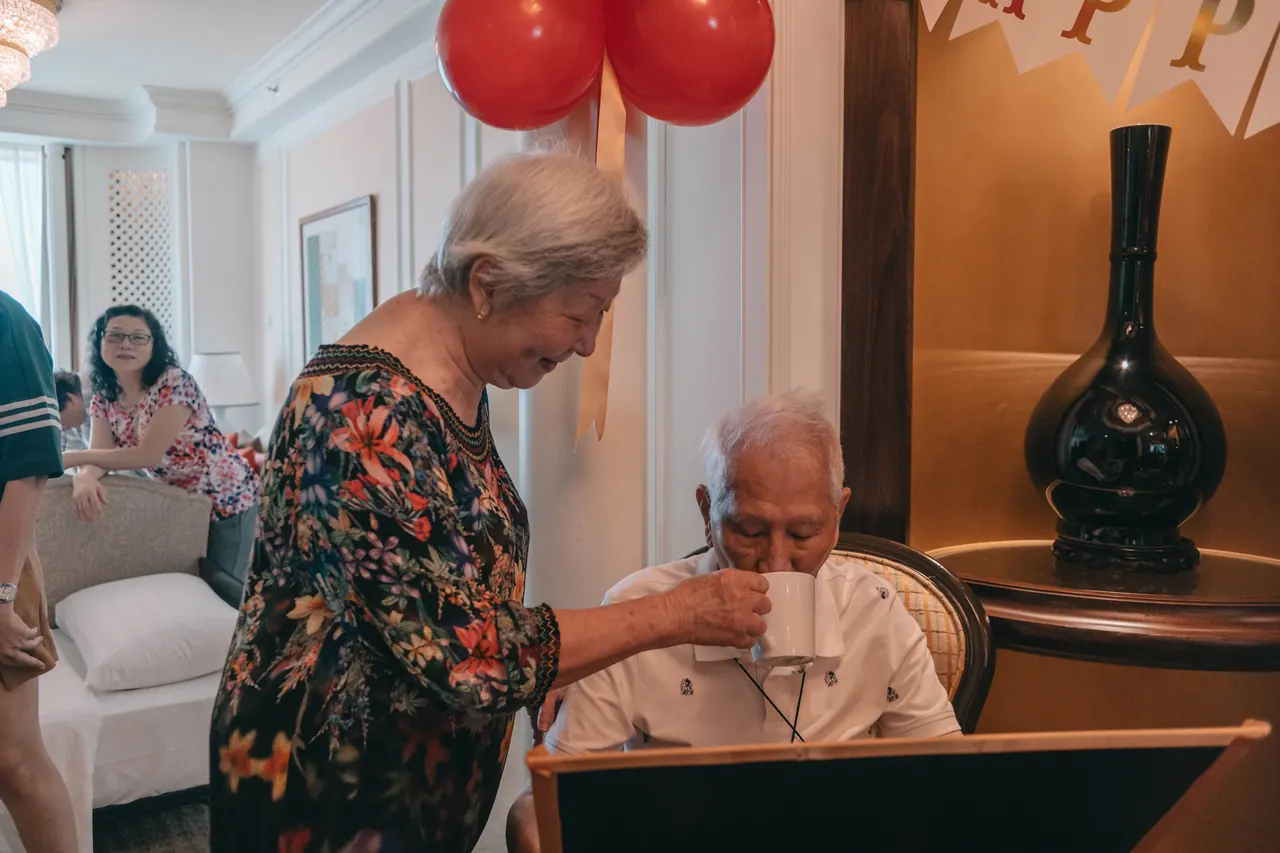 An older woman leans in to an older man at the table.