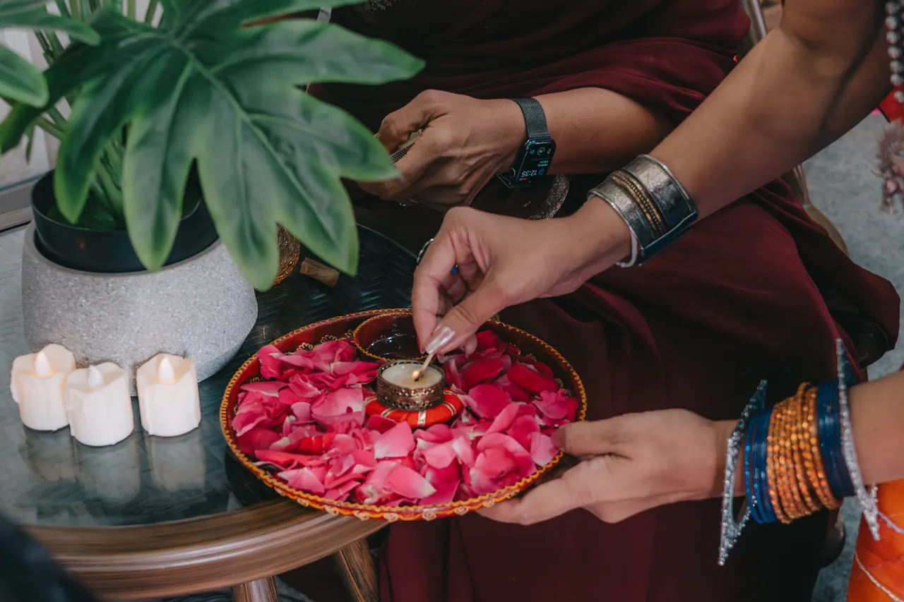 Hands scatter rose petals from a brass tray.