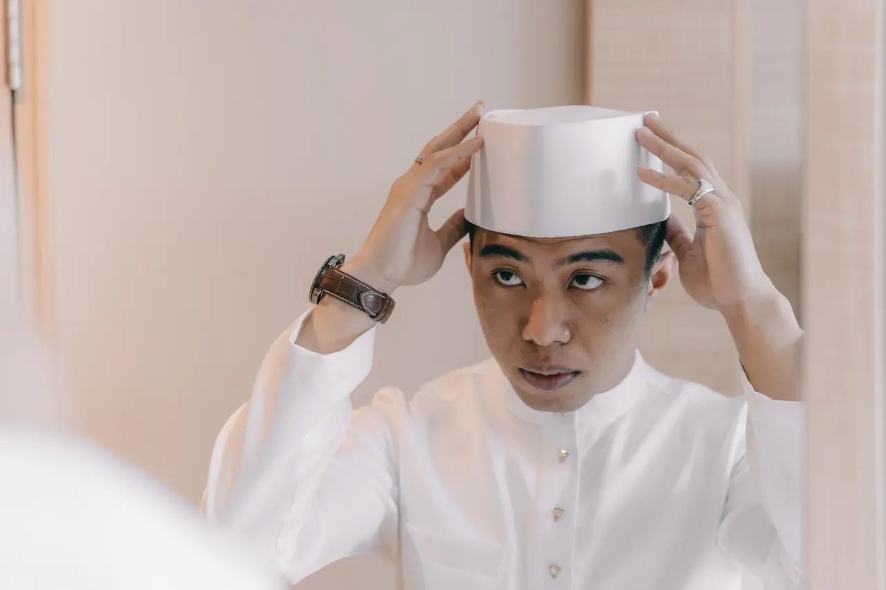 The groom adjusts his white songkok.