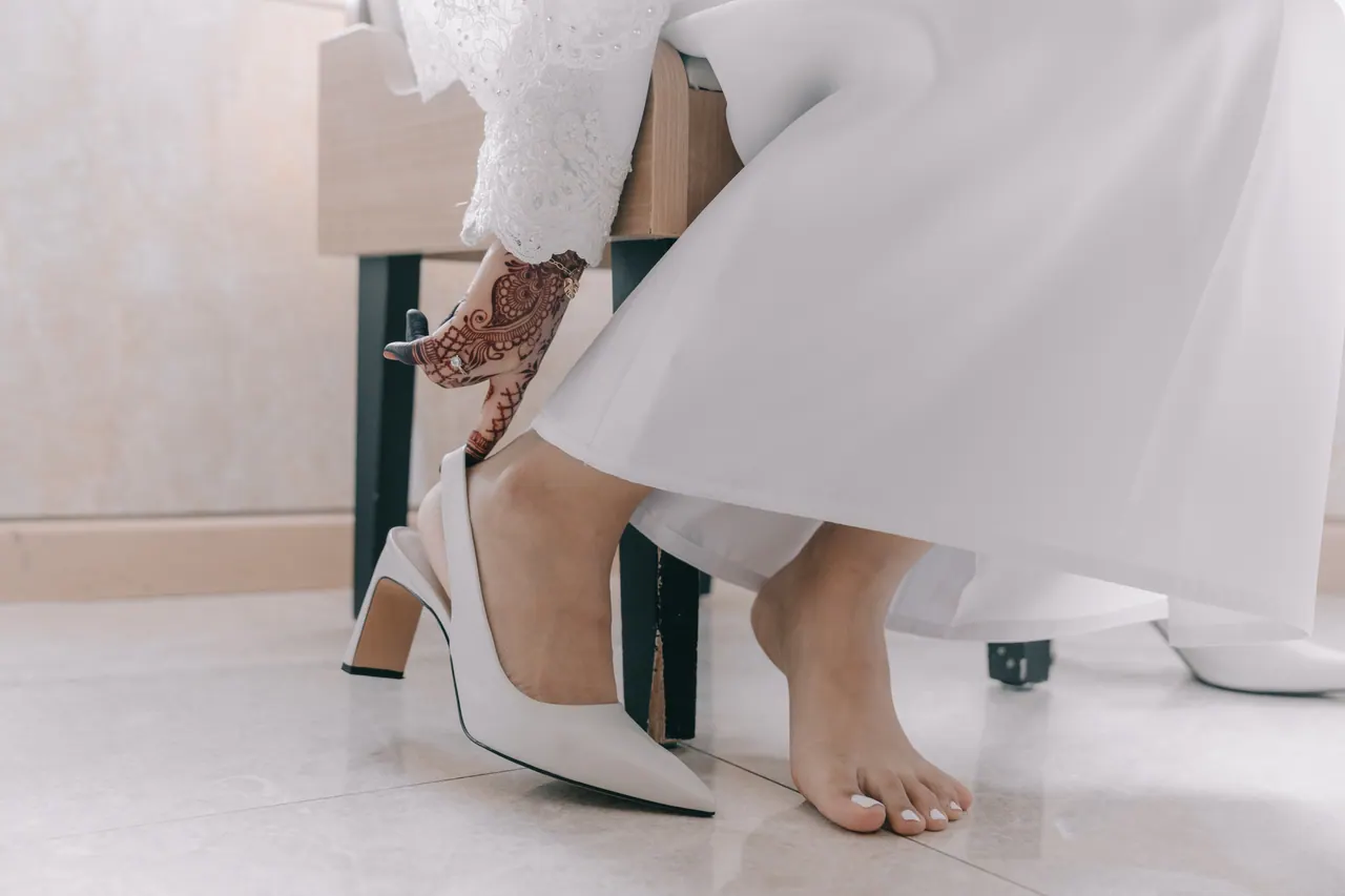 The bride slips on a white heel, her hands painted with henna.