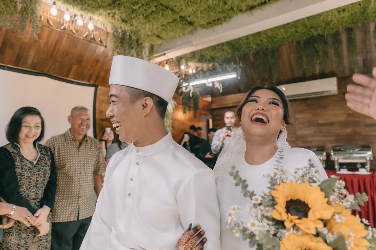 The couple laugh as they walk in, guests around them.