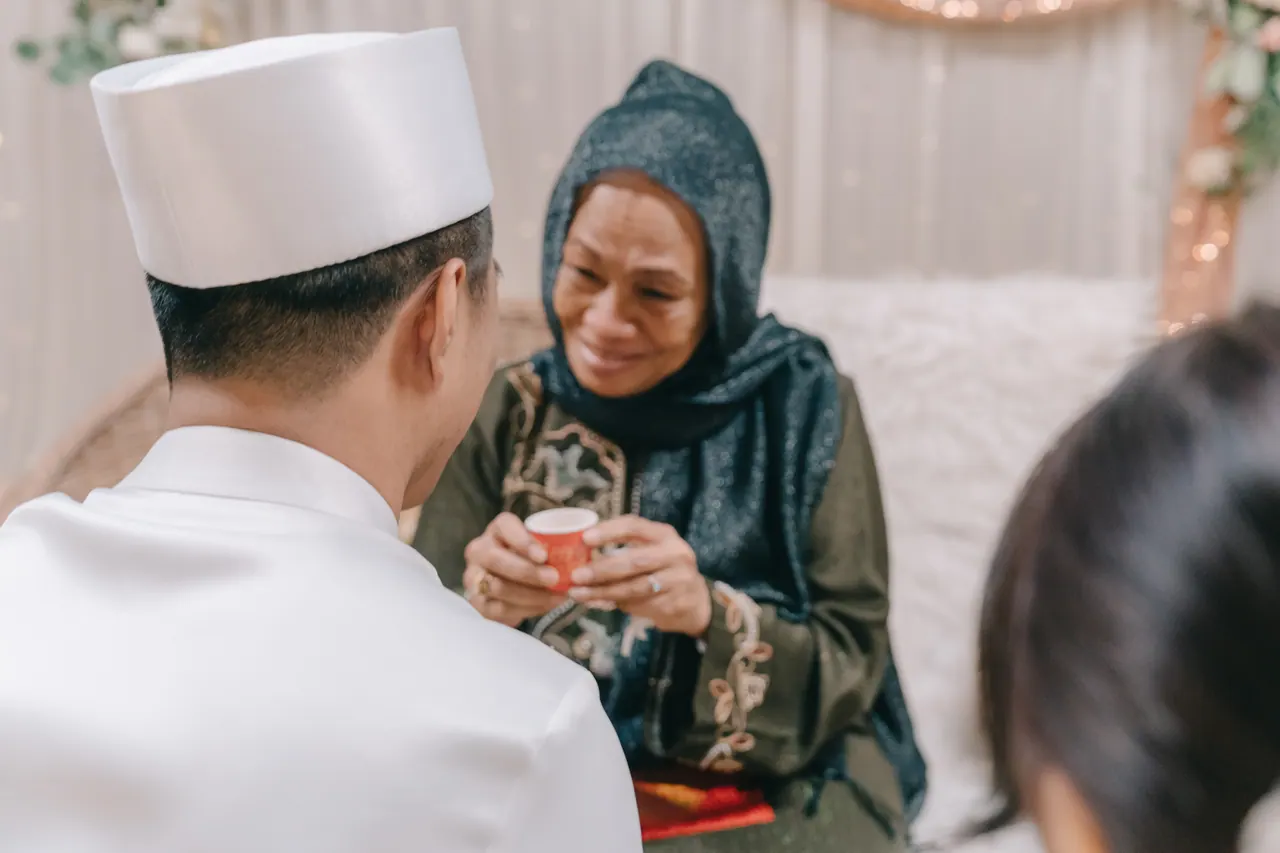 An older woman smiles as the groom serves her tea.