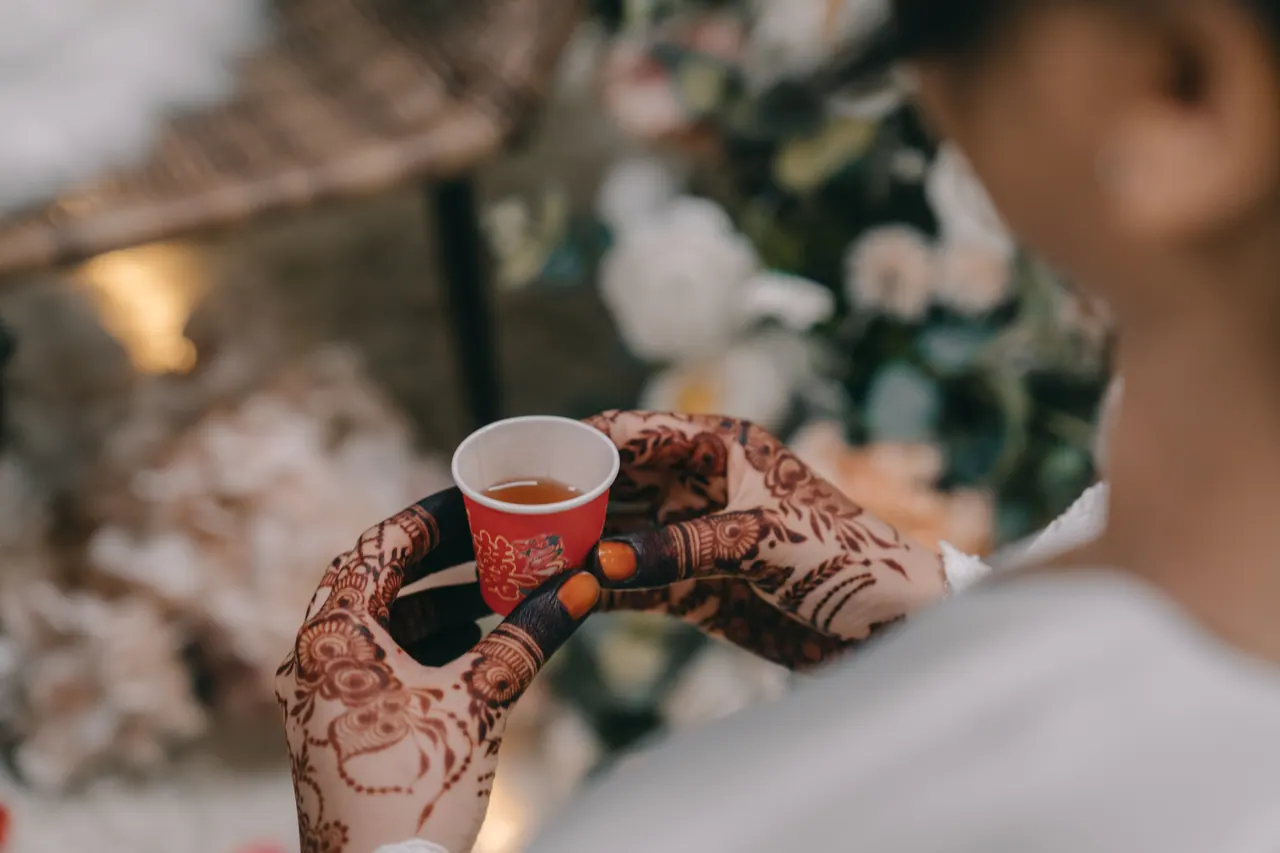 A hennaed hand holds a small red cup.