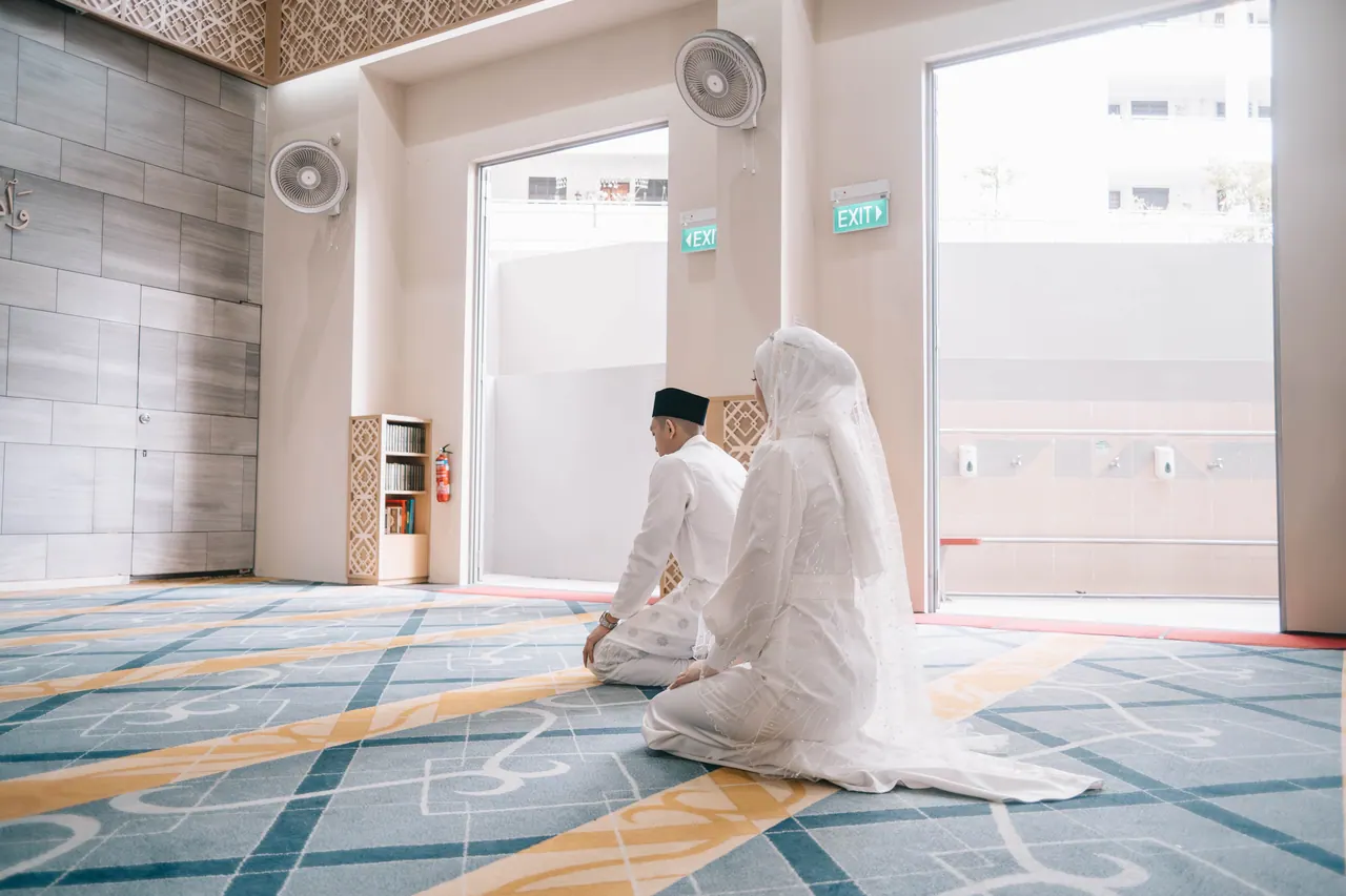 The couple kneel on a patterned carpet in a bright hall.