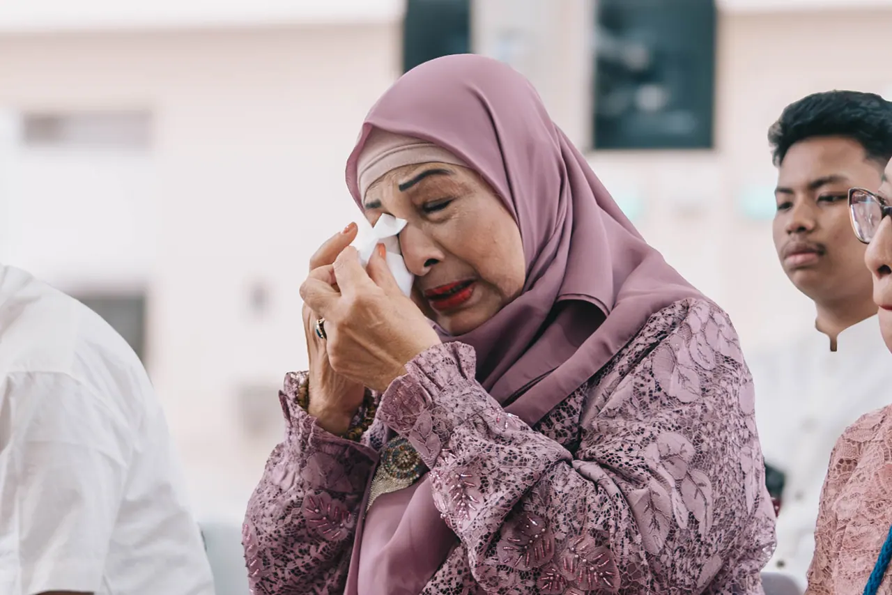 An older woman in purple wipes away tears.