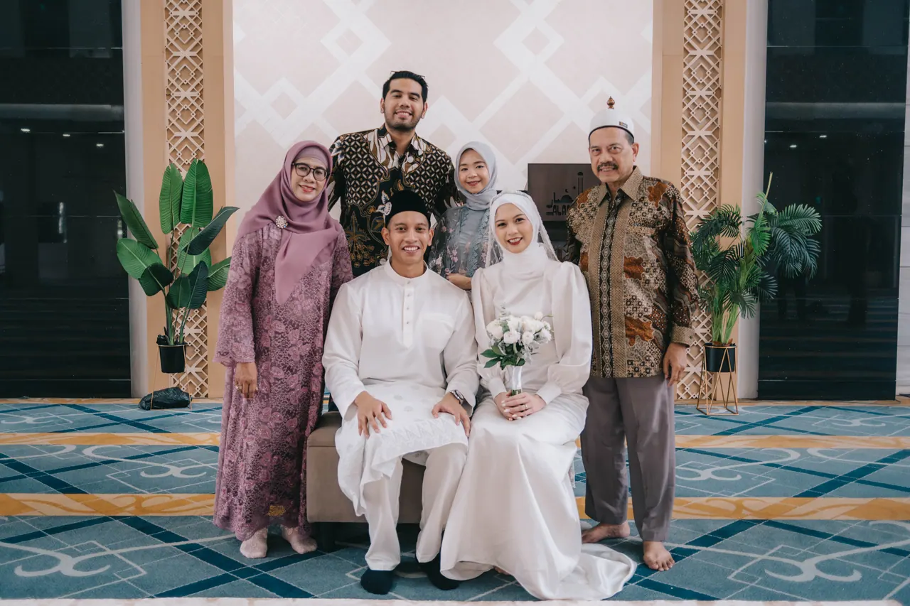 The couple seated with their parents beneath the arch.