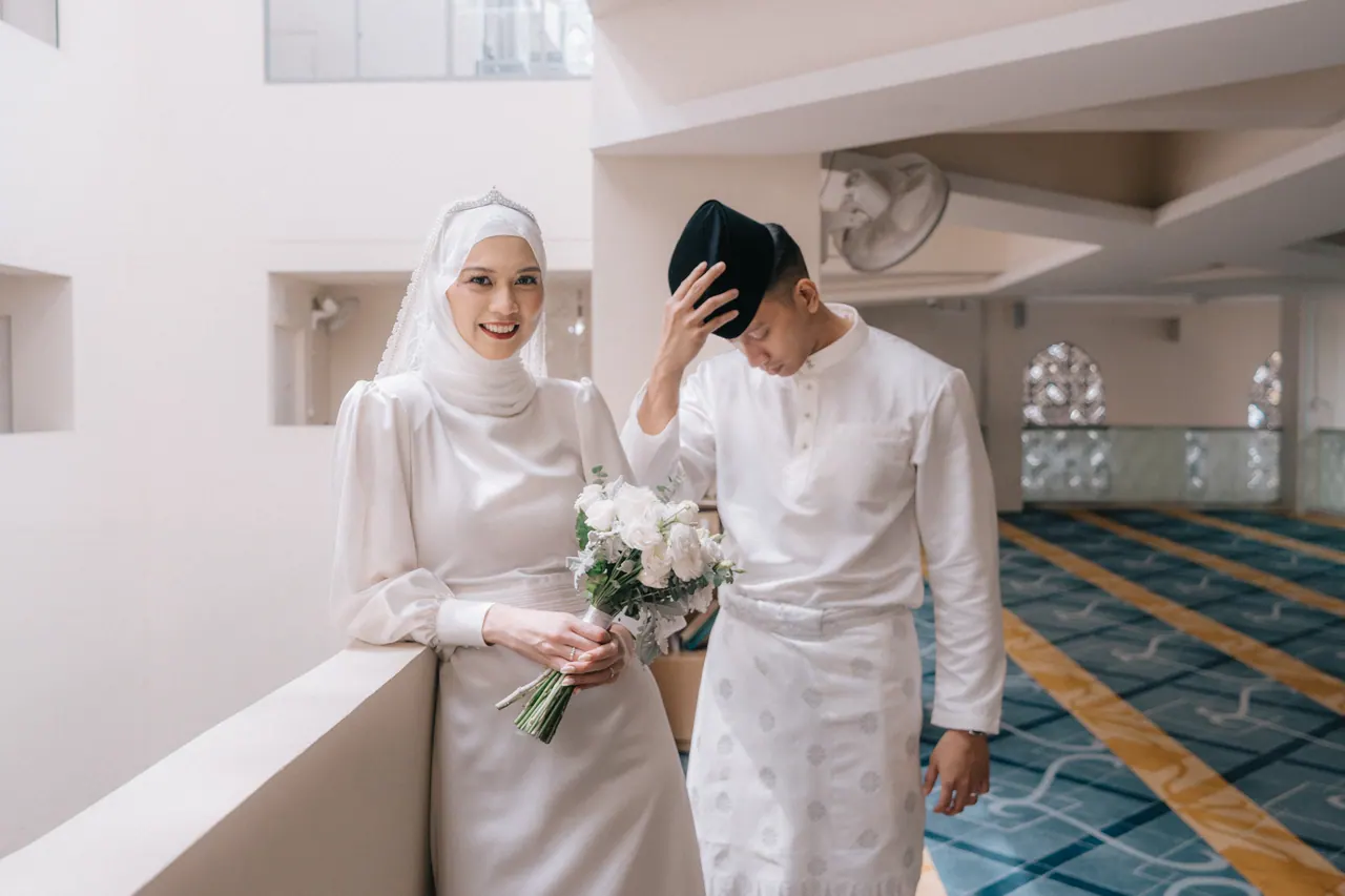 The bride smiles with her bouquet as the groom covers his face with his hand.